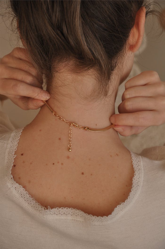 Close-up of a woman fastening a delicate gold necklace, showcasing elegance and style.