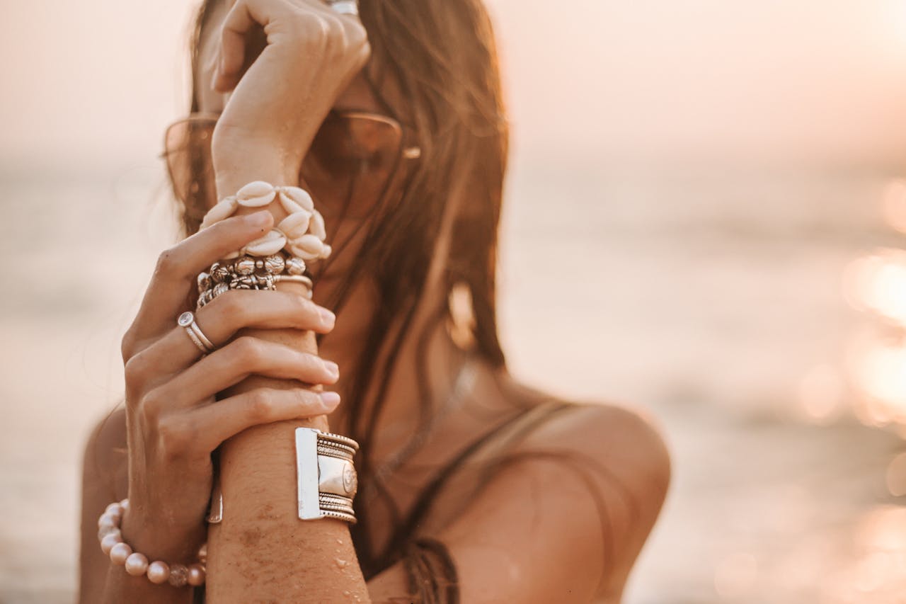 A woman posing with stylish jewelry on a beach during sunset.